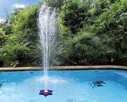 Pool fountain in action with water spraying high into the air, surrounded by greenery.